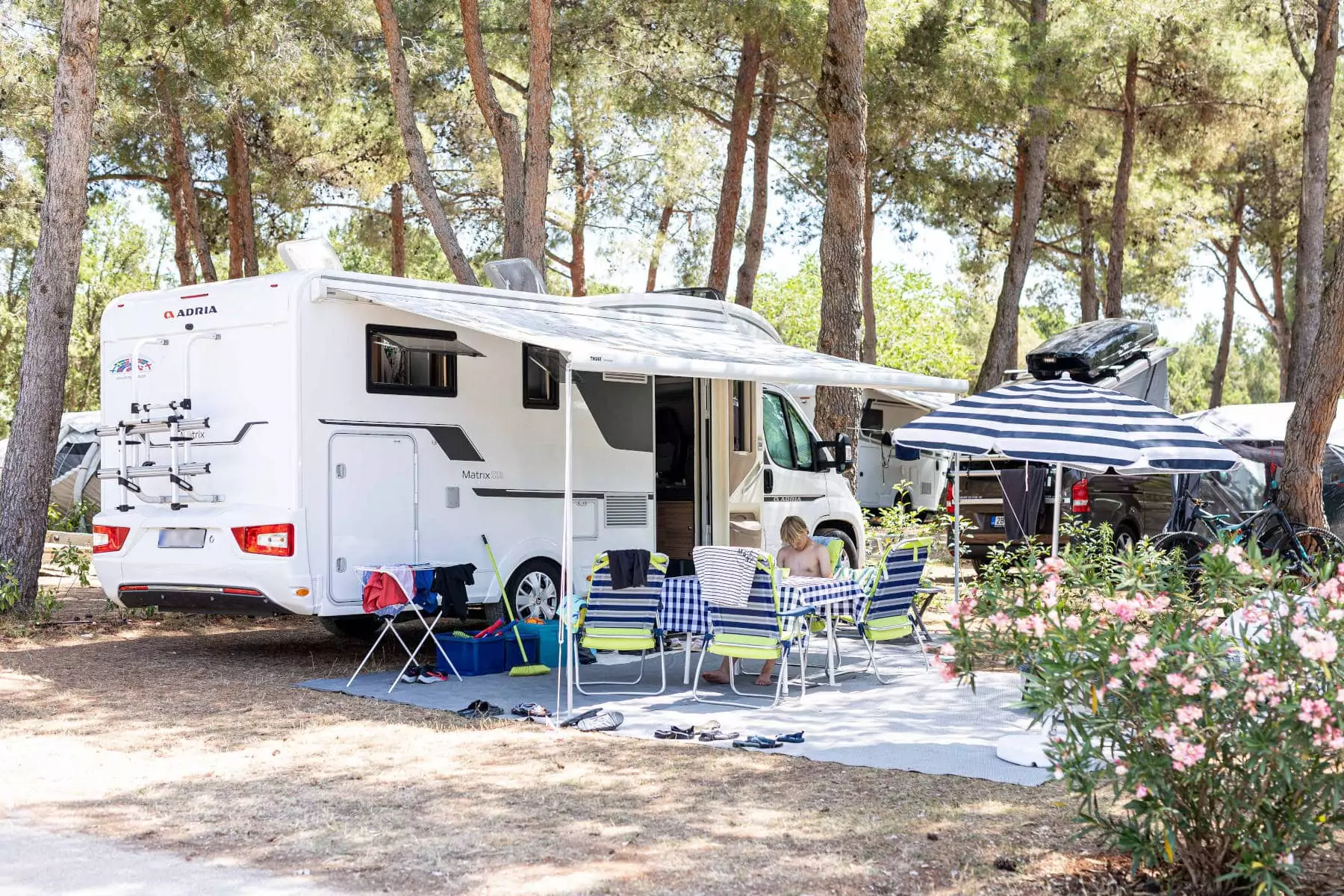 ragazzo seduto sotto tenda davanti al camper nella piazzola del villaggio vacanze bivillage