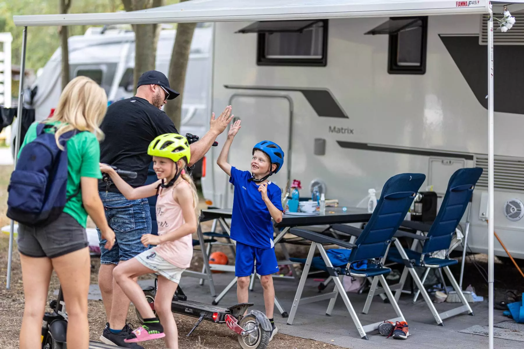 famiglia felice con bambini su monopattino davanti al camper in piazzola garden al bivillage