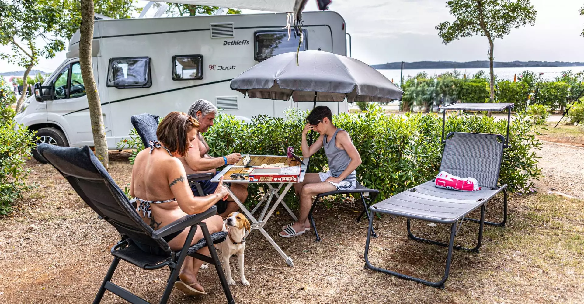 famiglia con cane seduta in piazzola premium mare nel campeggio bivillage