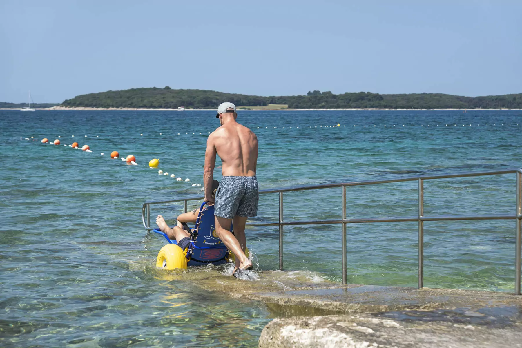 ragazzo in carrozzina che scende la rampa per disabili sul mare della Croazia presso il BiVillage