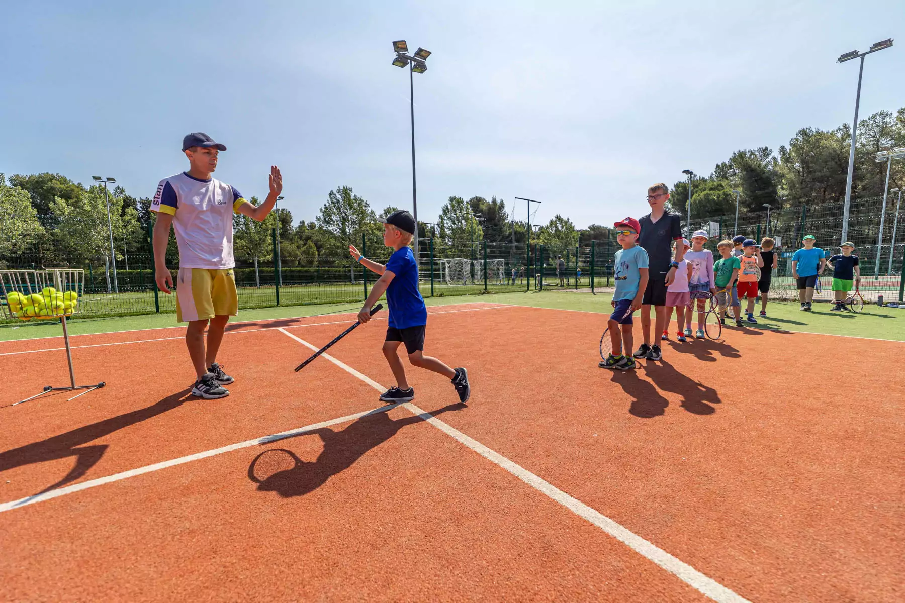 bambini in fila con istruttore di tennis