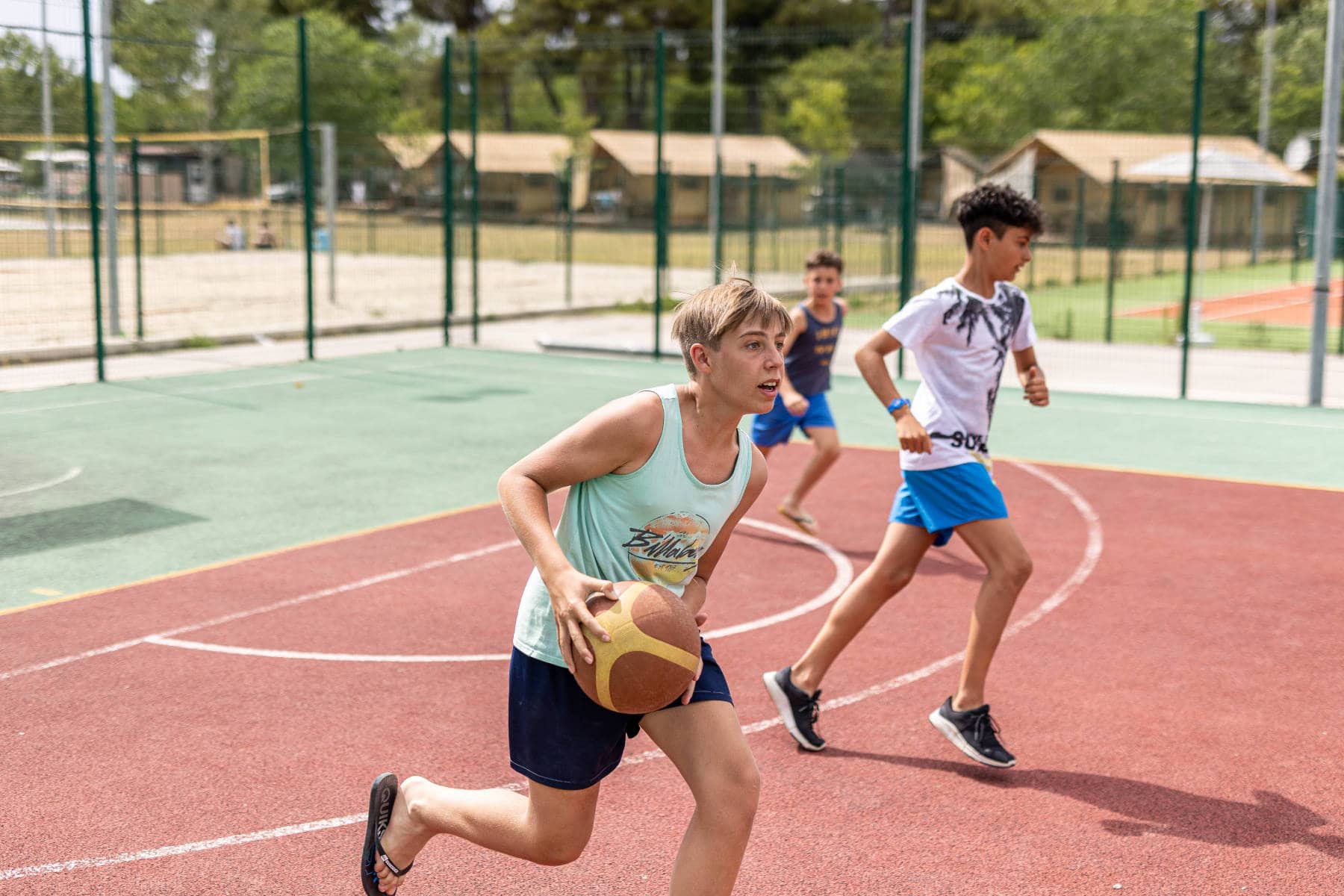 Campo da basket al bivillage ragazzo con palla da basket che corre