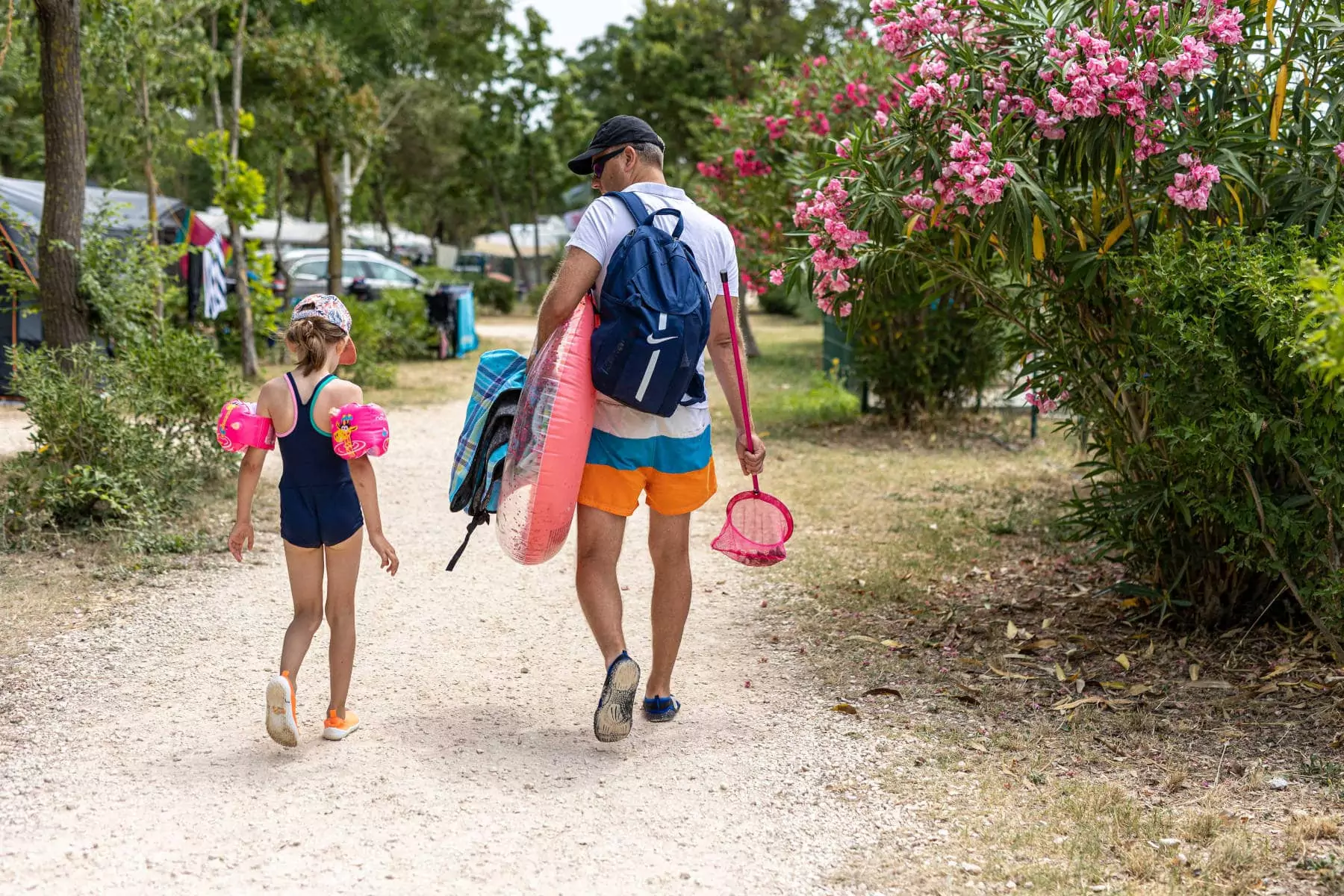 papà e bambina cammina nel campeggio con braccioli salvagenti e giochi per la spiaggia