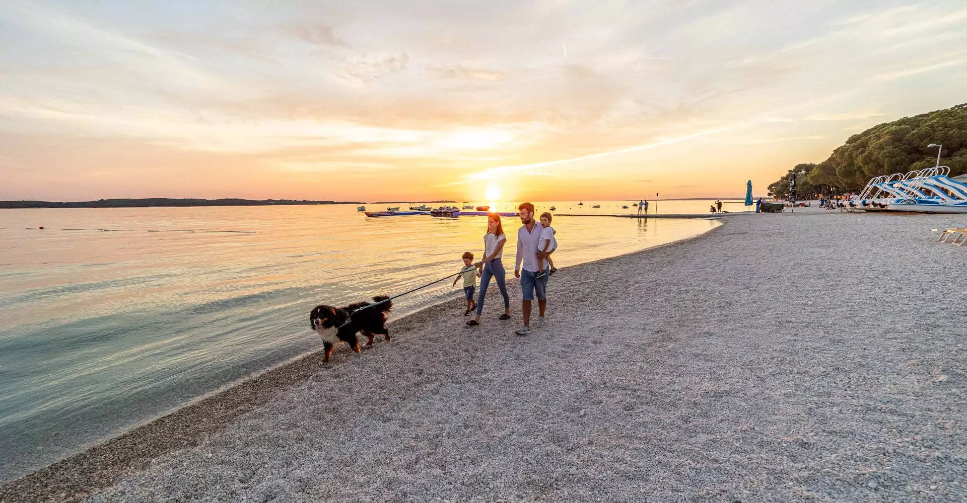 famiglia con bambini e cane che passeggia al tramonto sul lungomare del bivillage