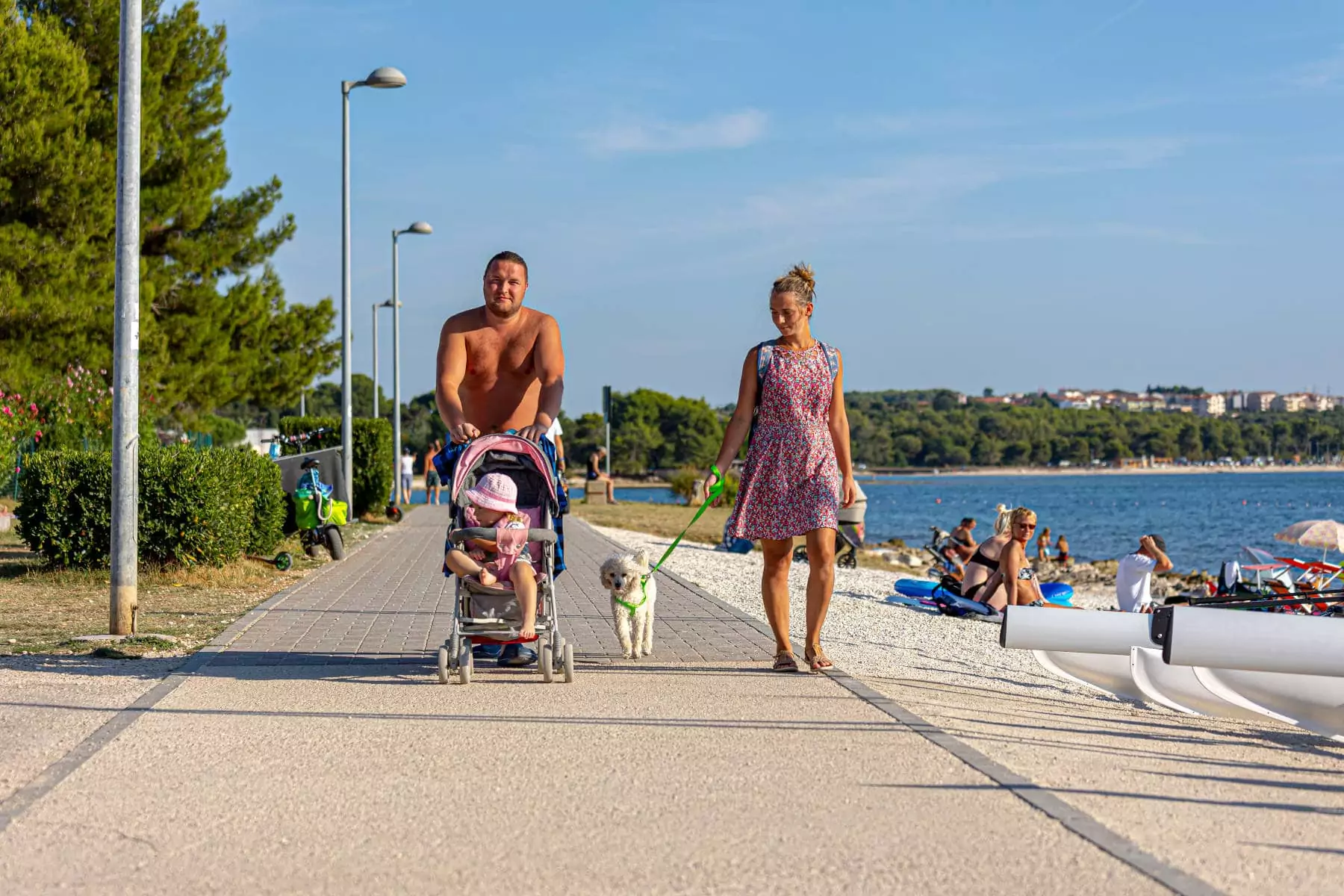 coppia con bimba nel passeggino e cane al guinzaglio che cammina sulla pista ciclo pedonale 